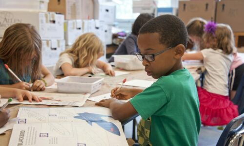 boy in green sweater writing on white paper