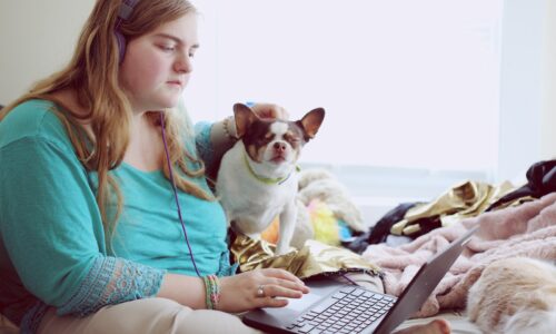 girl in blue jacket holding white and brown short coated puppy